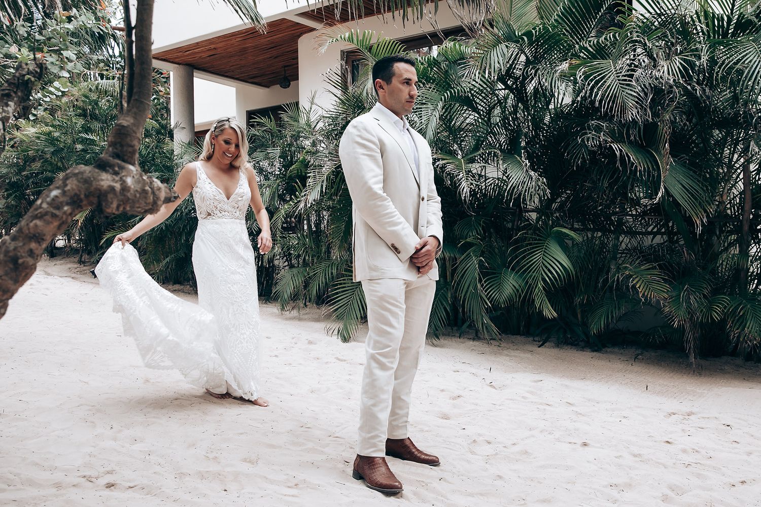 A wedding couple in white attire poses together in a lush tropical garden setting for their special day photos.