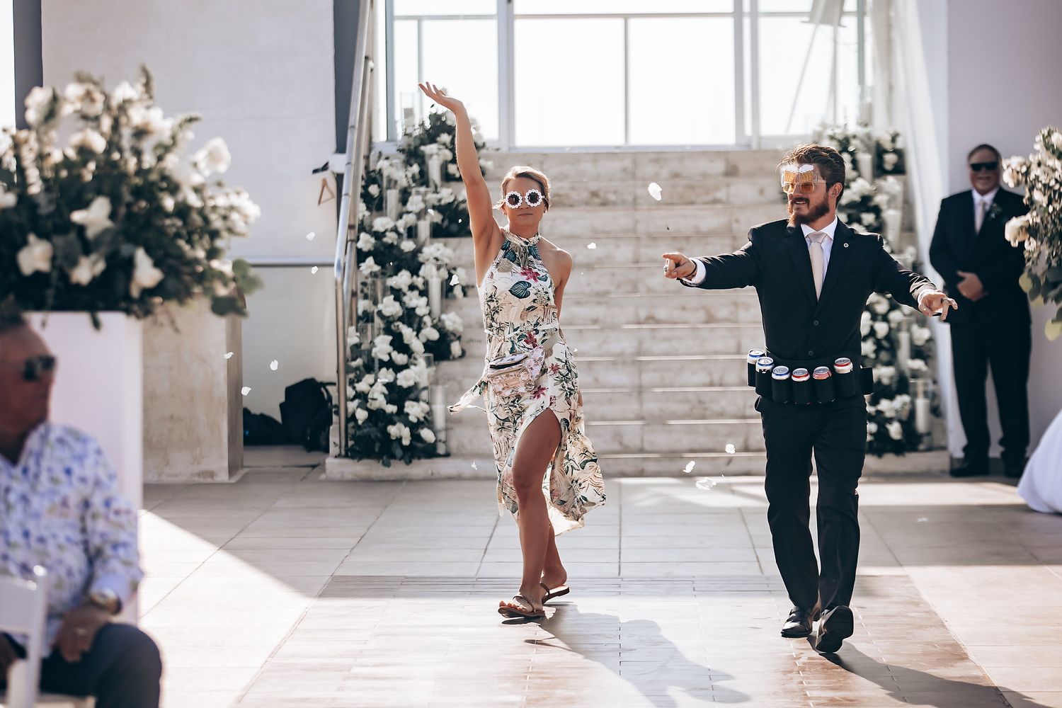 Wedding ceremony scene in bright indoor venue with white floral arrangements and elegant decor.