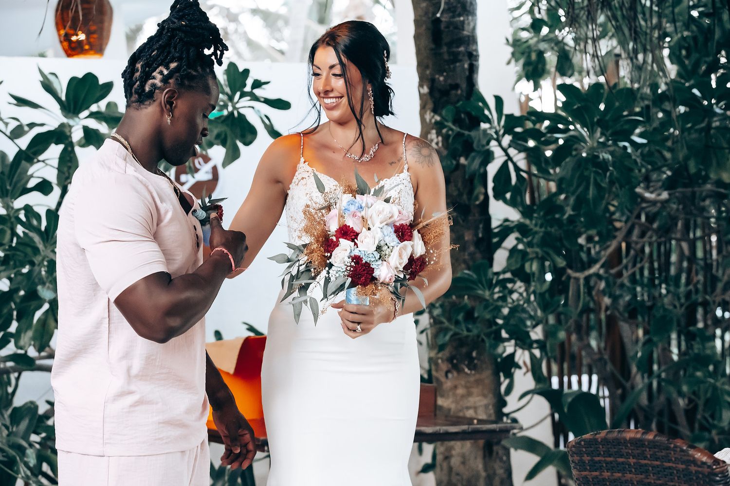 A bride and groom embrace during their tropical wedding ceremony surrounded by lush greenery.