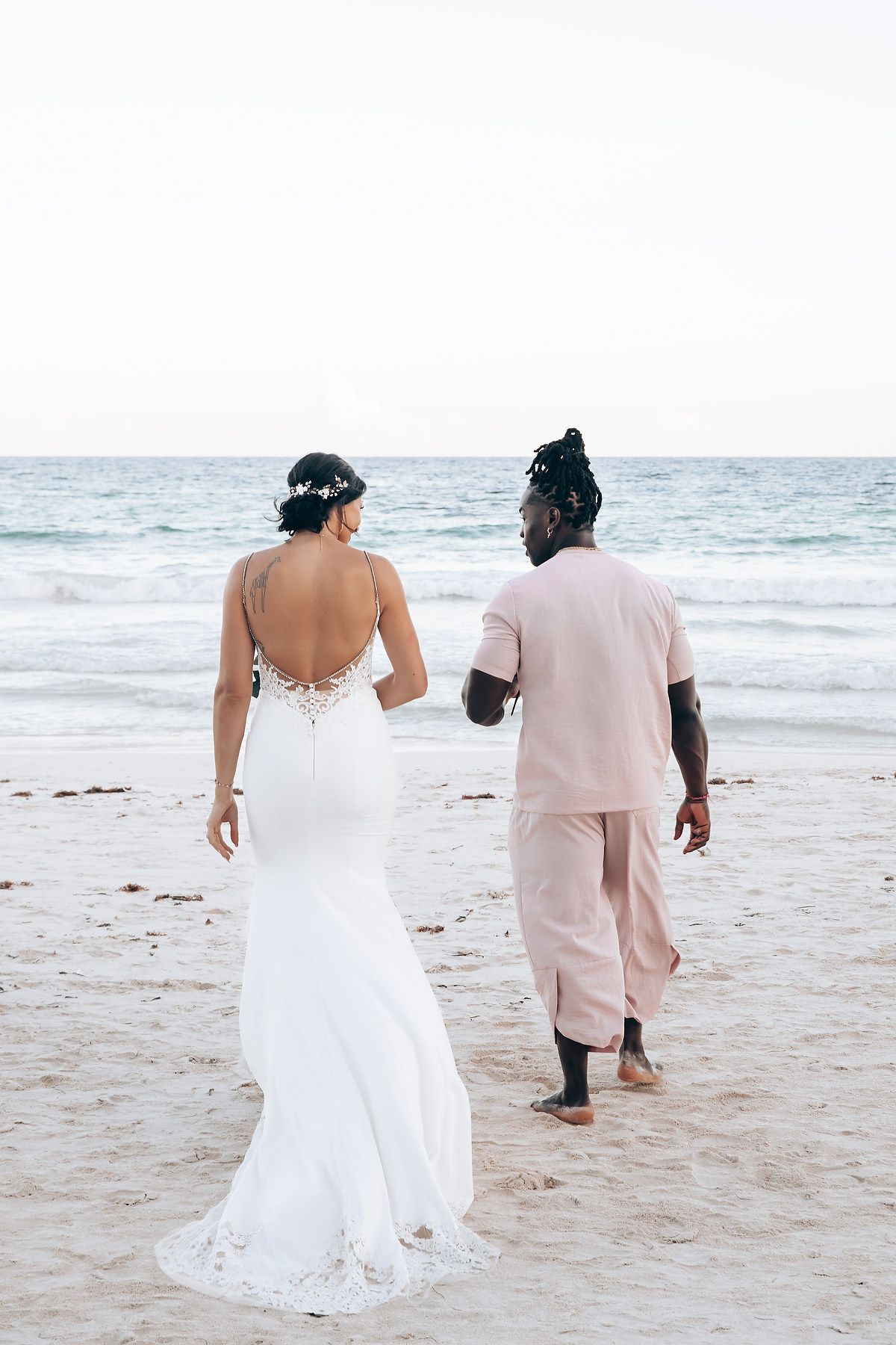A couple walks on a tropical beach, the woman wearing a white wedding dress.