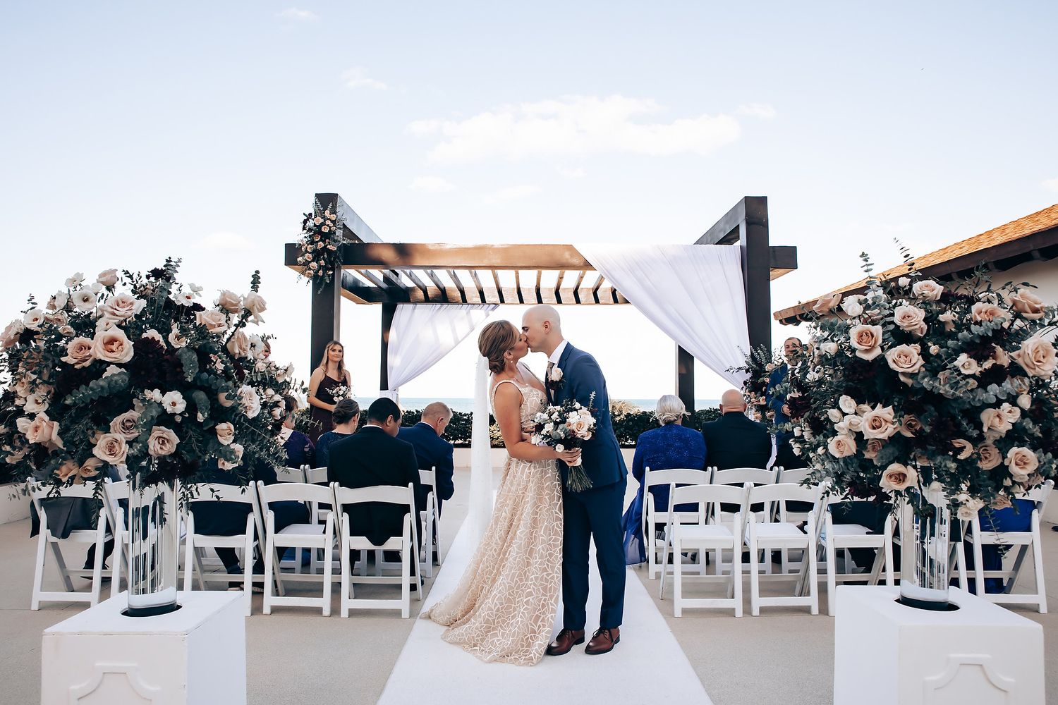 A bride and groom stand together in an elegant outdoor wedding ceremony with floral arrangements.