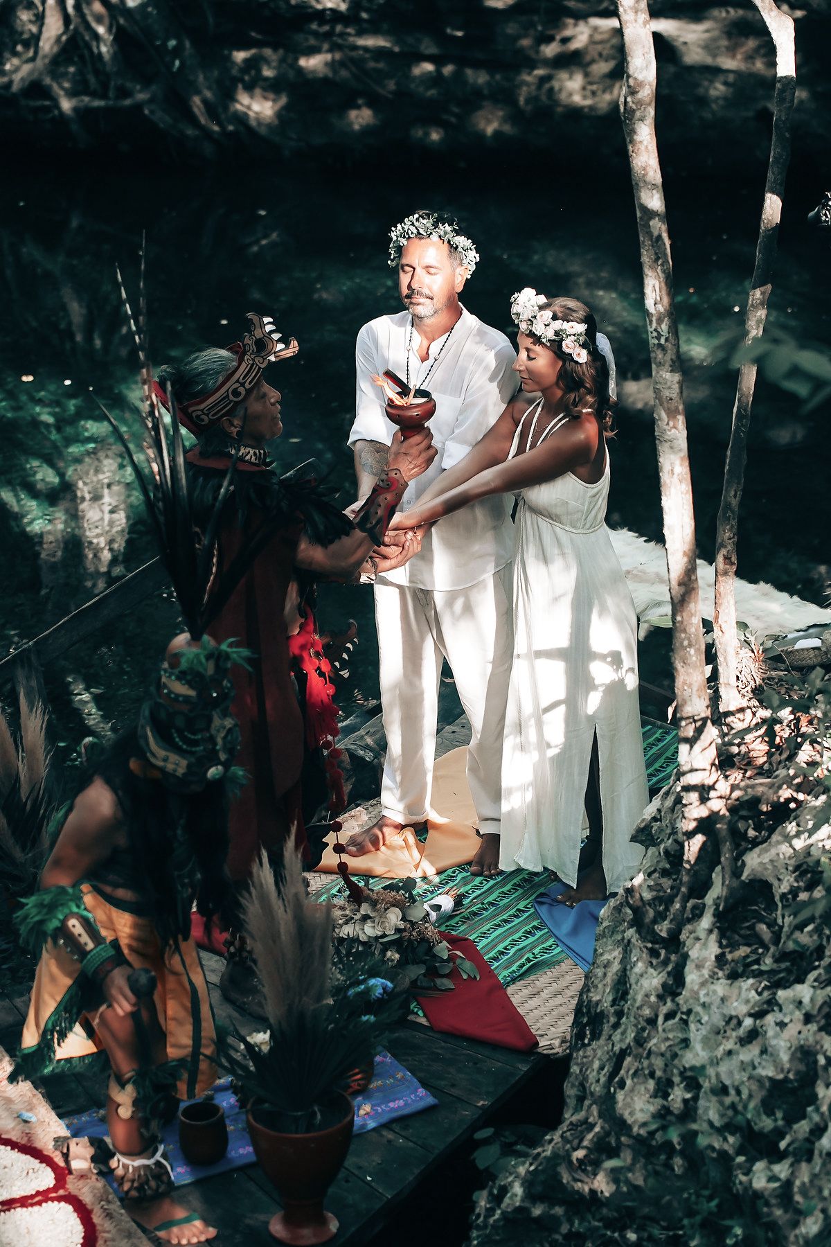 A wedding ceremony takes place in a natural, outdoor setting with a couple and other individuals present.