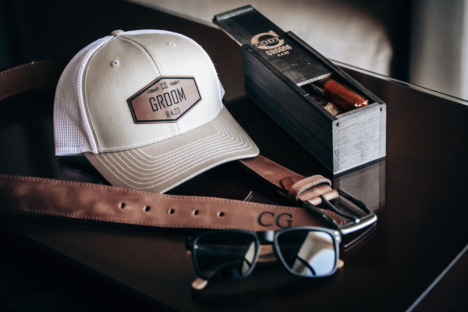 An image displaying various accessories including a white baseball cap, sunglasses, and a leather case.