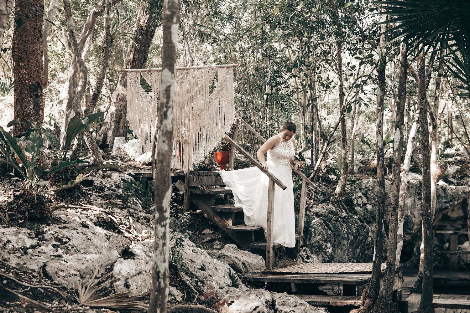 A person dressed in traditional indigenous attire standing on a wooden platform in a forested setting.