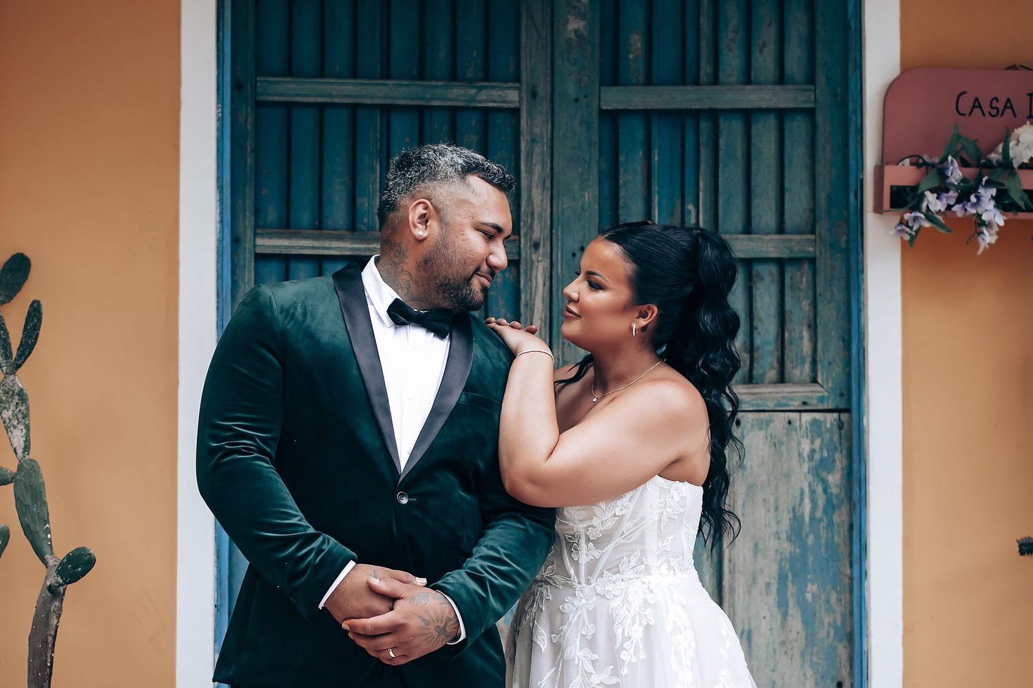 A couple in elegant wedding attire share a tender moment in front of vintage turquoise doors.