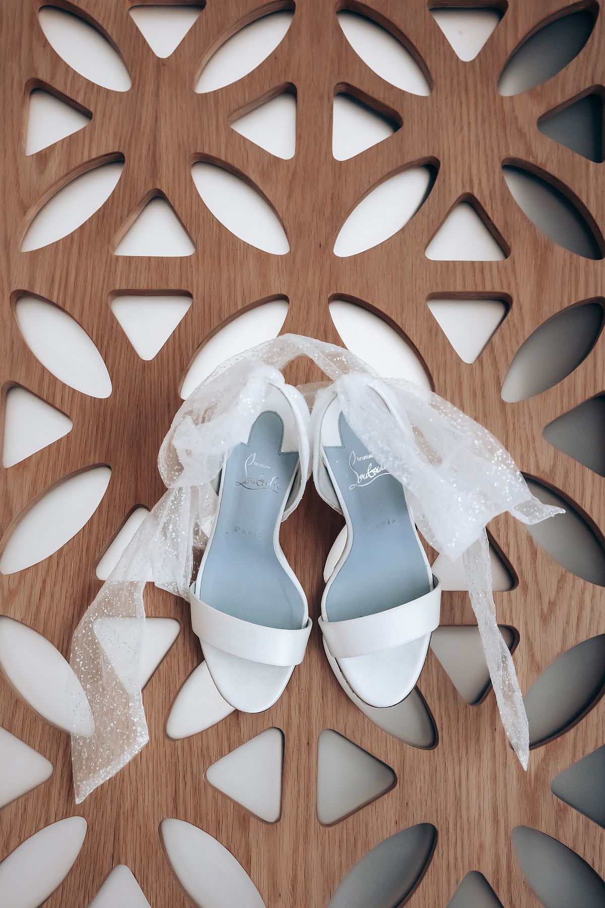 White wedding shoes displayed against a decorative wooden lattice background.