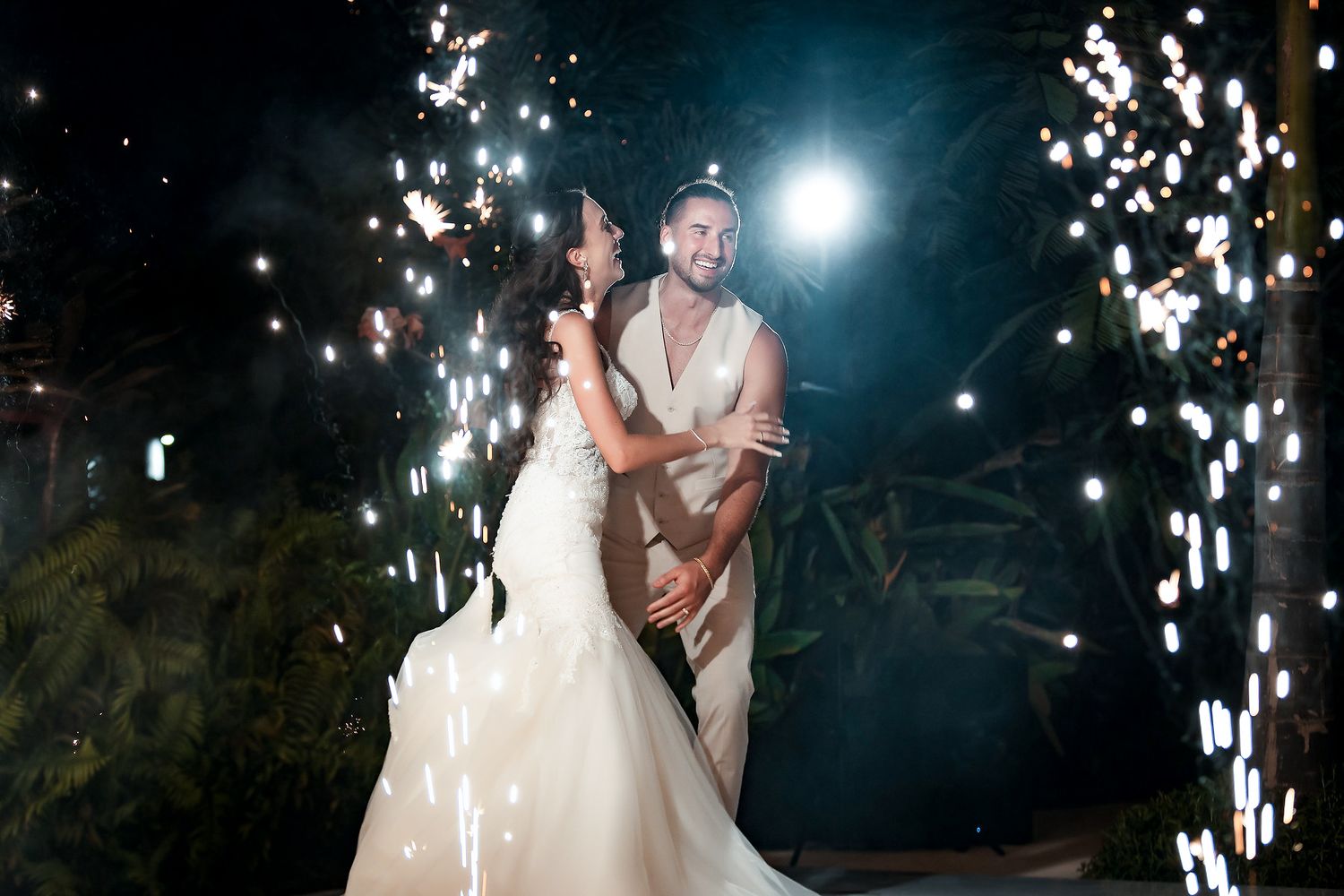 Bride and groom share romantic first dance surrounded by sparkling fireworks at elegant outdoor night wedding celebration.