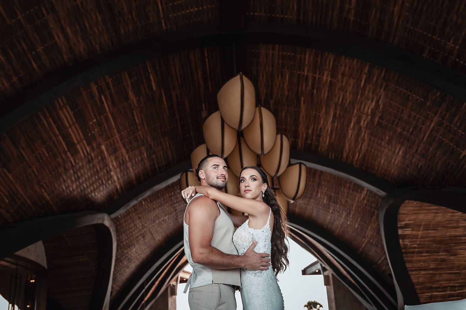 Couple embracing under ornate wooden arched ceiling in tropical resort setting.