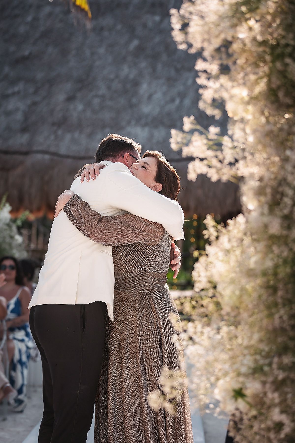 A couple shares a heartfelt embrace at an outdoor wedding ceremony surrounded by white floral arrangements.