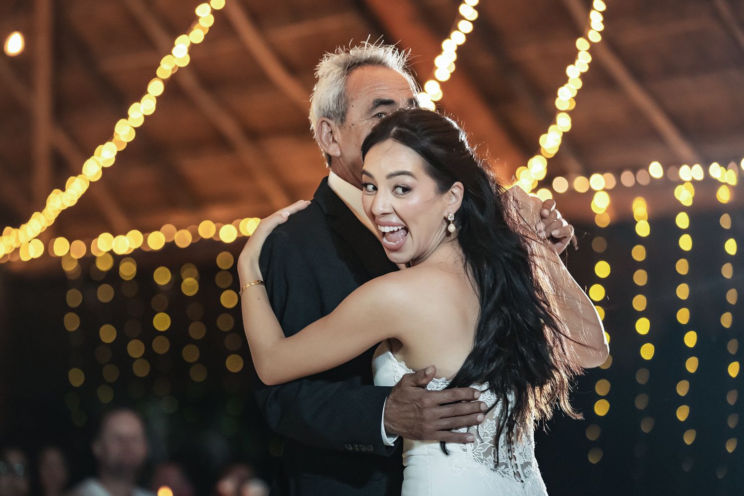 Bride and her father share a joyful father-daughter dance under warm string lights at a wedding reception.