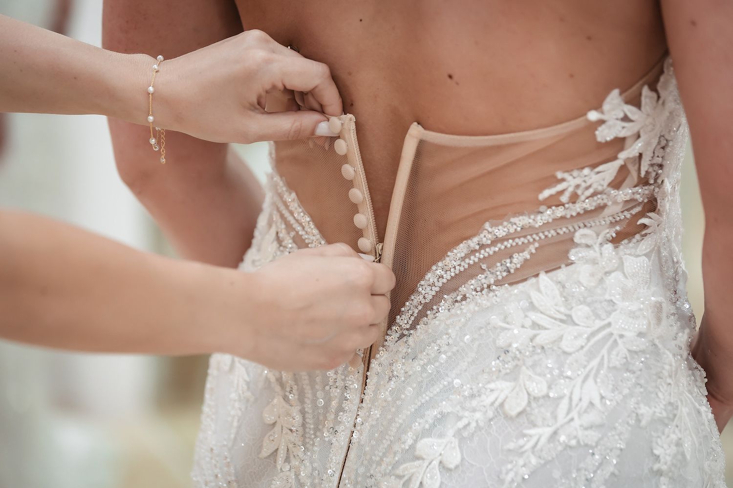Bride getting lace wedding dress buttoned up the back by a bridesmaid before the ceremony.