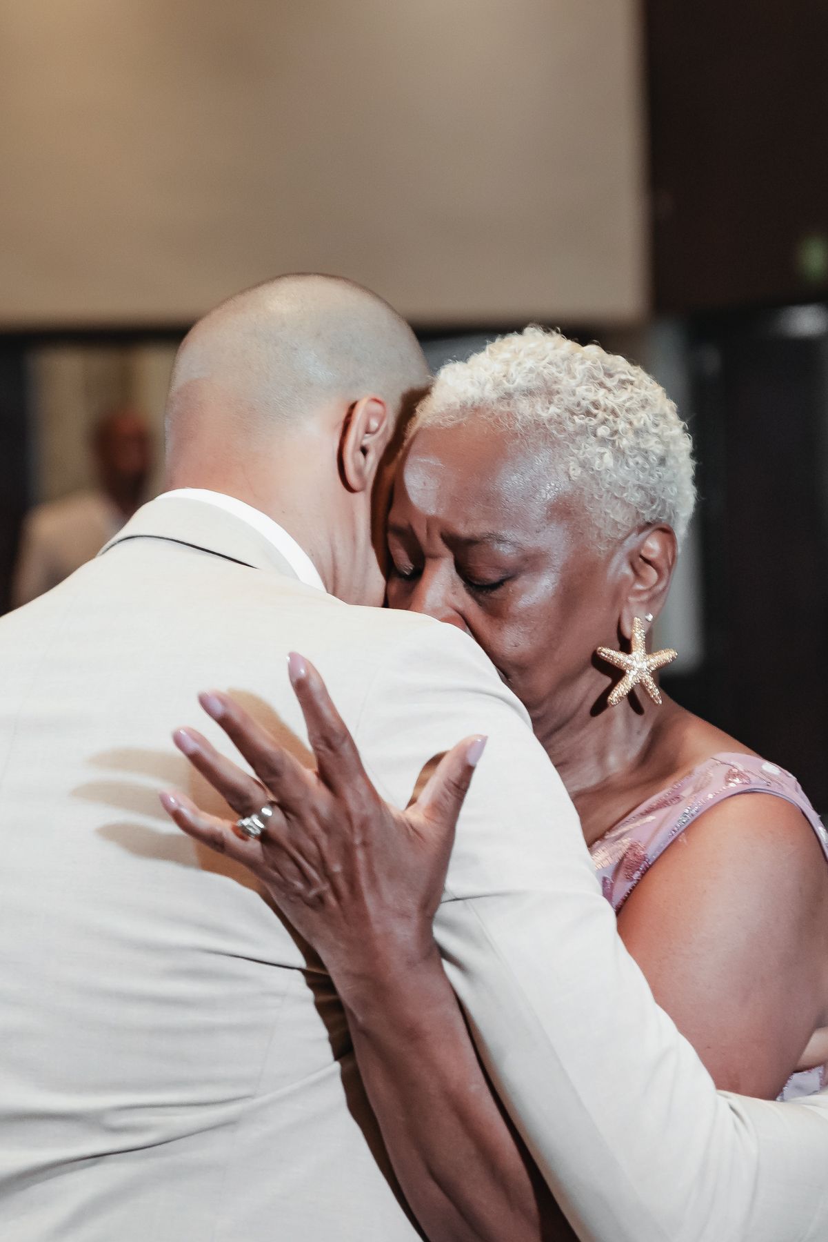 A groom and his mother share a tender embrace during the mother-son dance at a wedding reception.