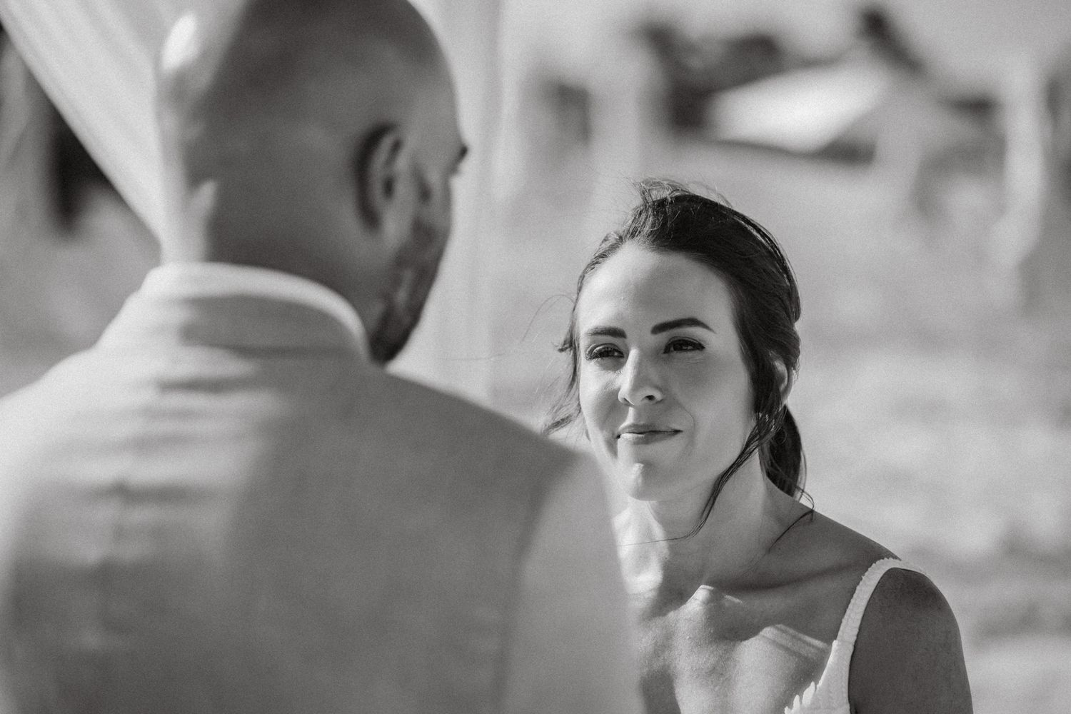 Black and white wedding photo of bride gazing lovingly at groom during ceremony.