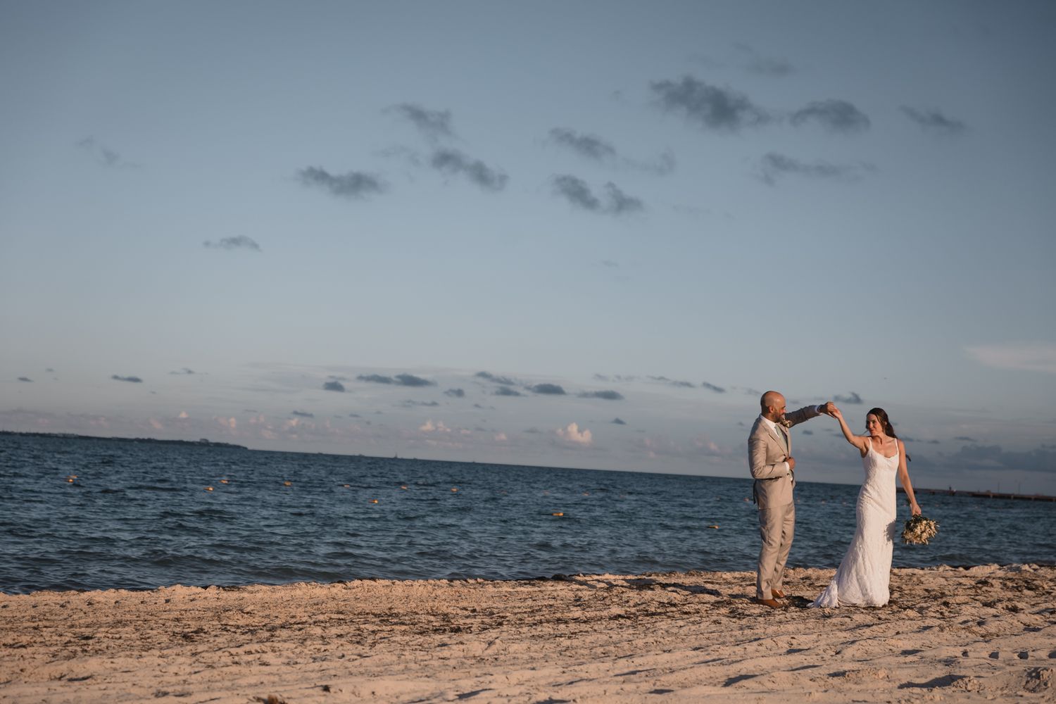 Bride and groom dancing on a sandy beach at sunset during their seaside wedding celebration.