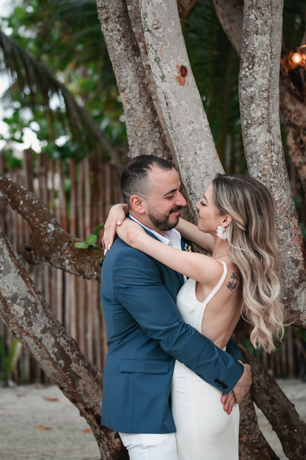 Bride and groom embrace romantically among palm trees in a tender beach wedding portrait.