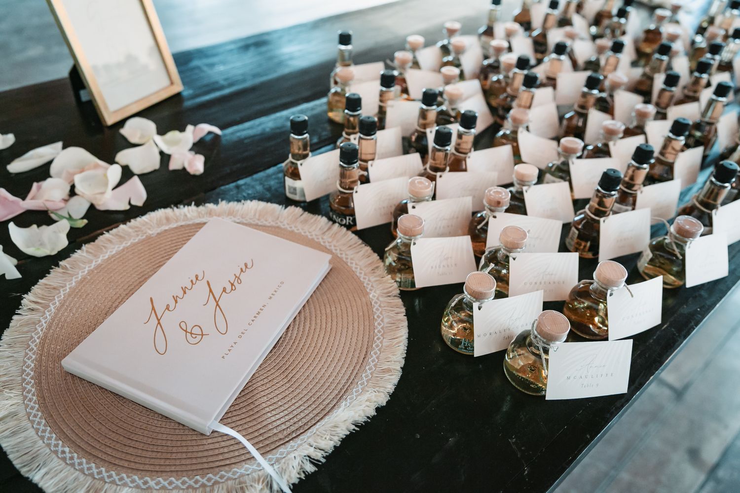 Wedding escort cards displayed with small bottle favors on a table beside a personalized guest book.