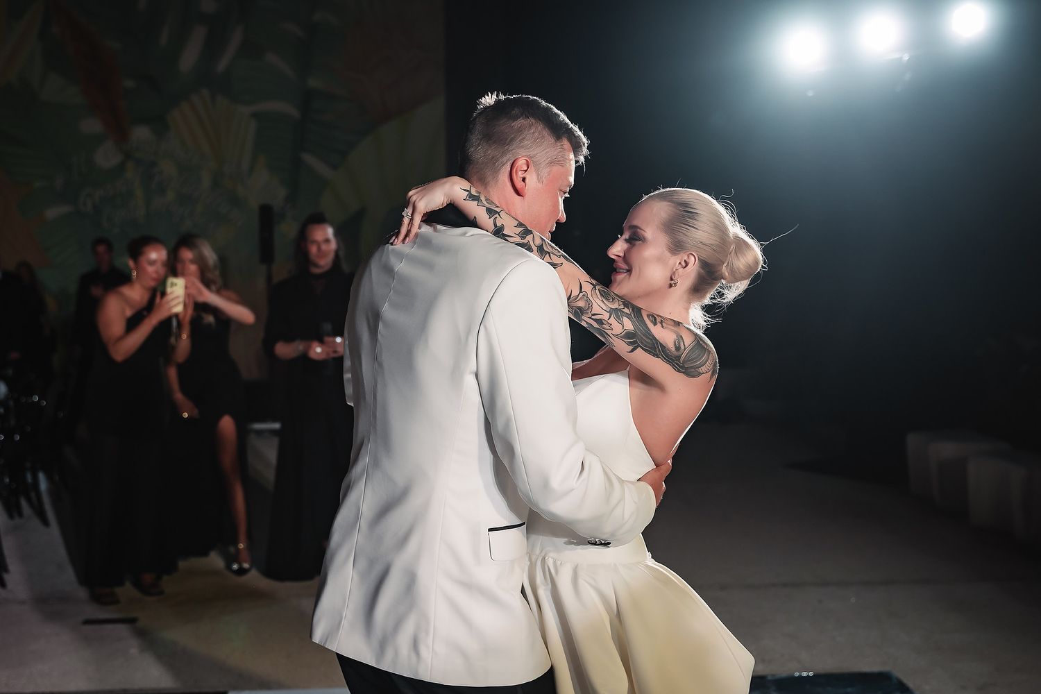Wedding couple dancing together during their first dance under dramatic spotlights in a dark reception venue.