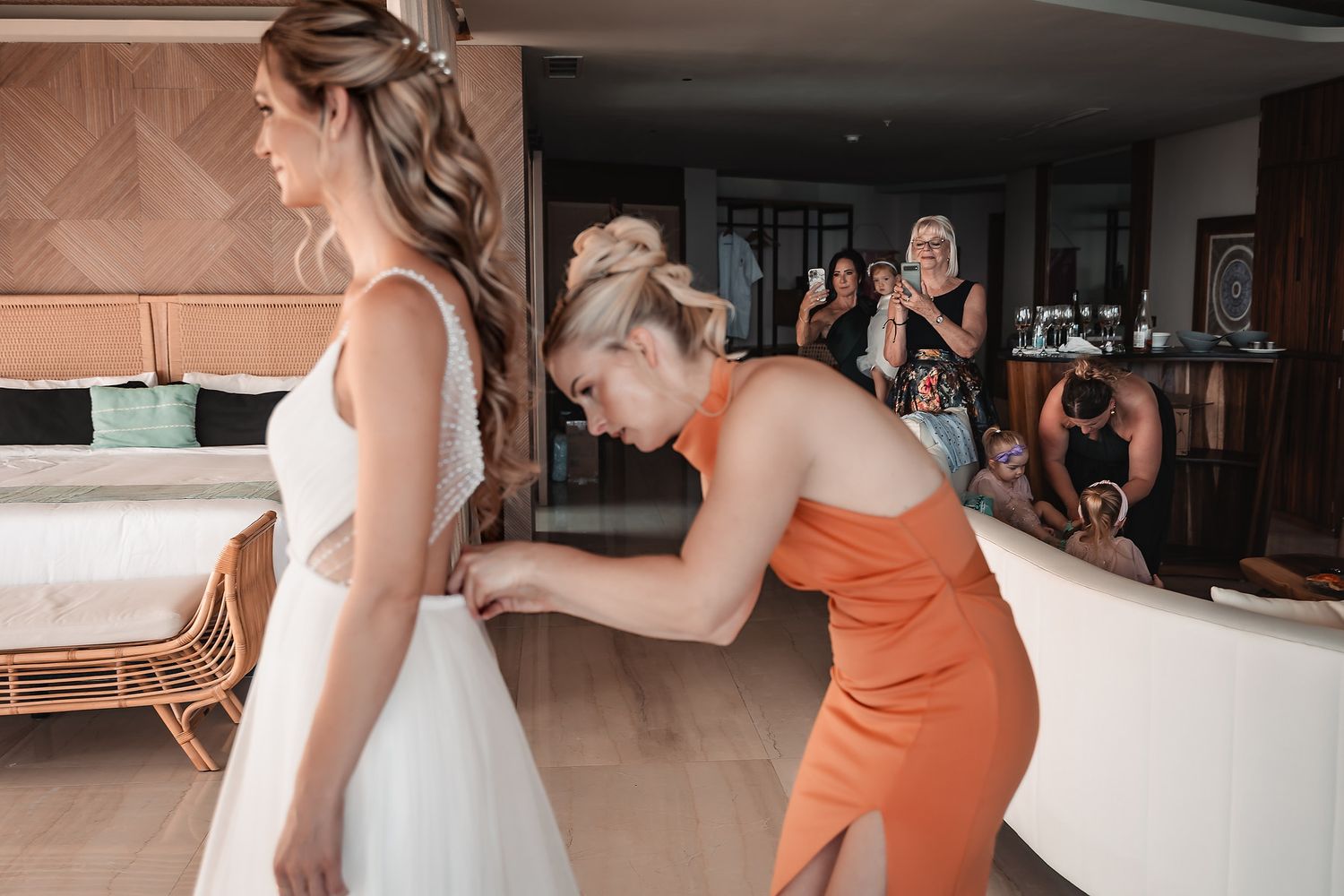 Getting ready scene with a white wedding gown being adjusted in a sunlit room.