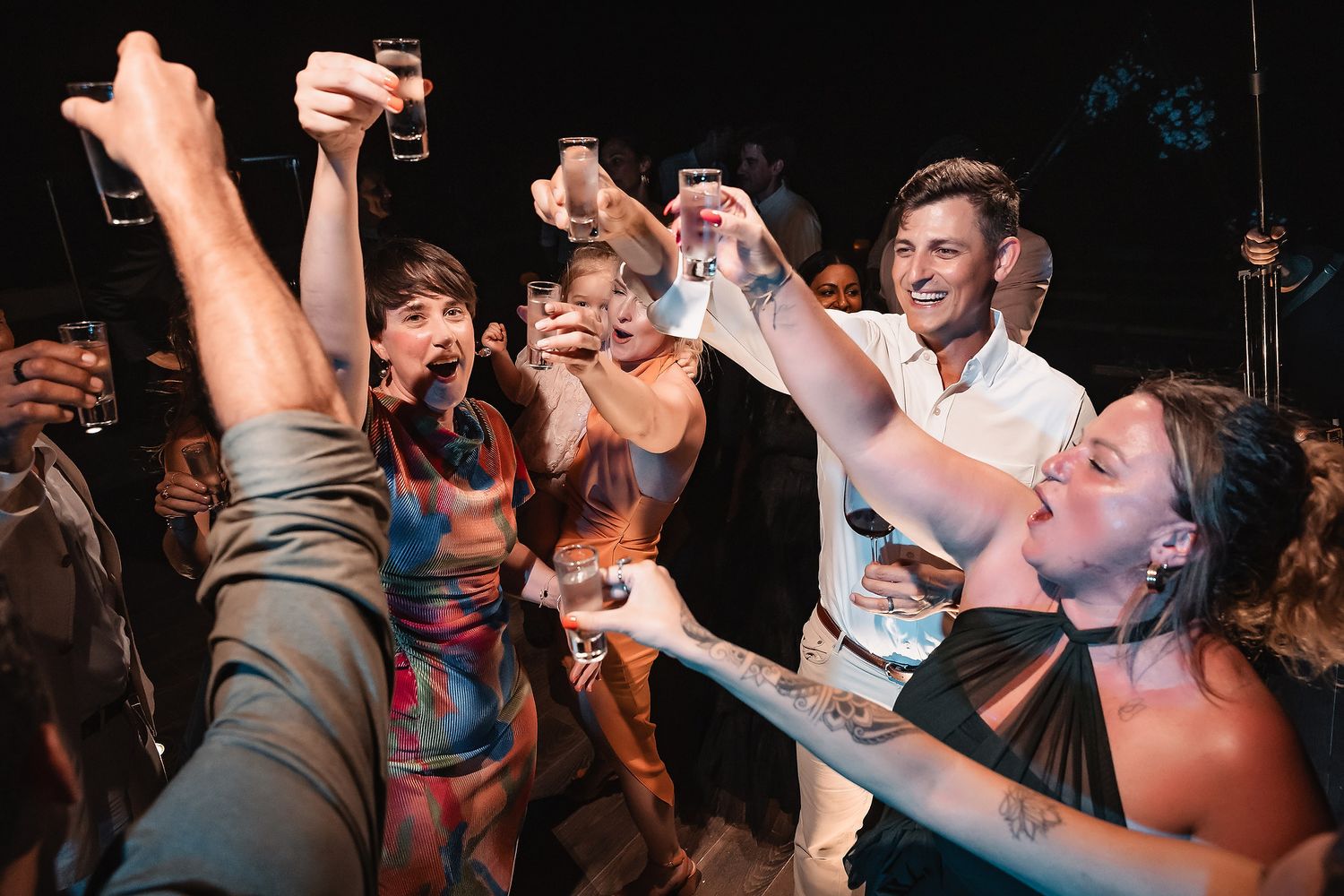 Party-goers dancing and raising their hands in celebration at a dimly lit venue.