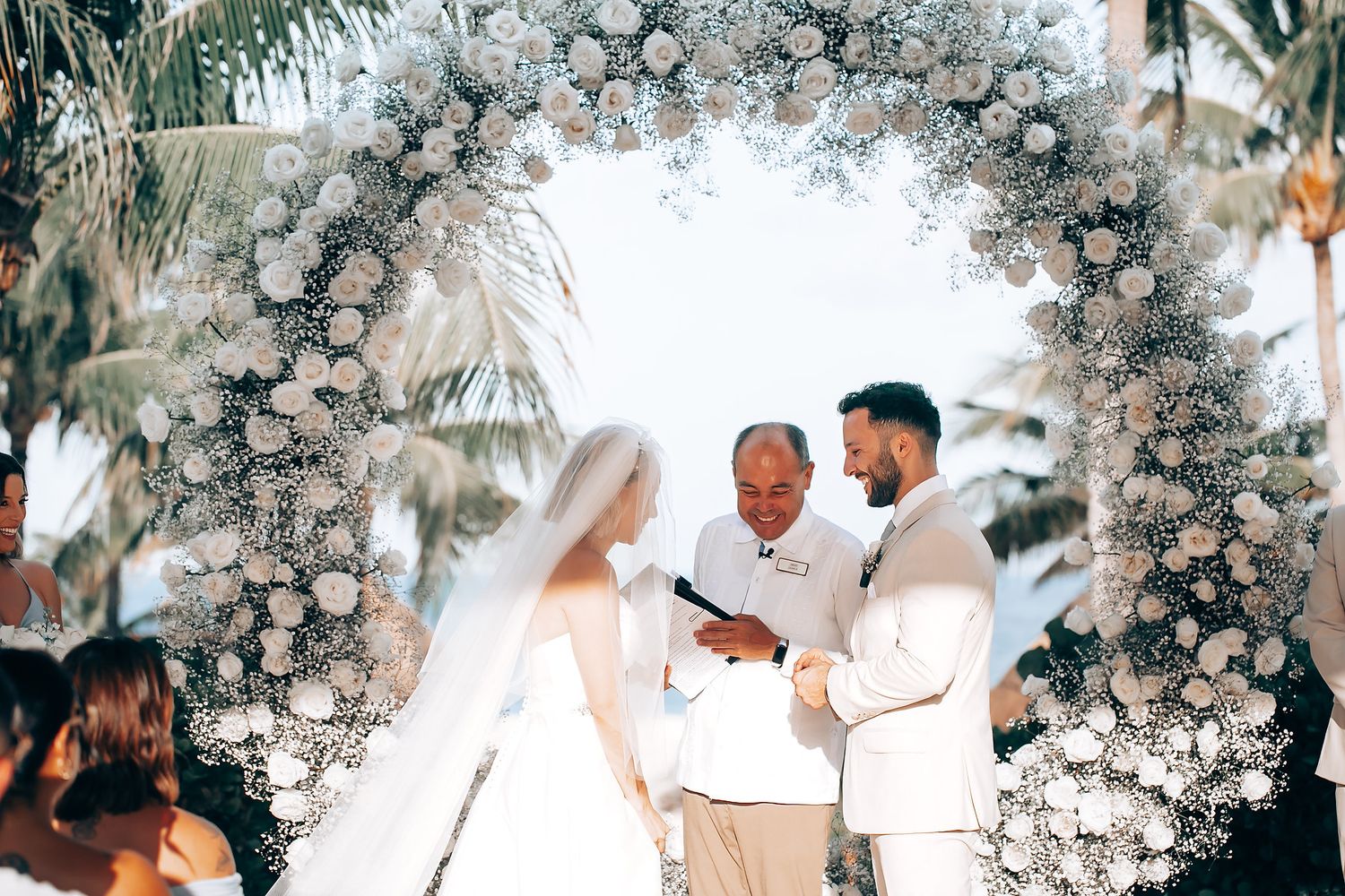 Beautiful wedding ceremony with white floral arch and tropical greenery creating a romantic atmosphere.