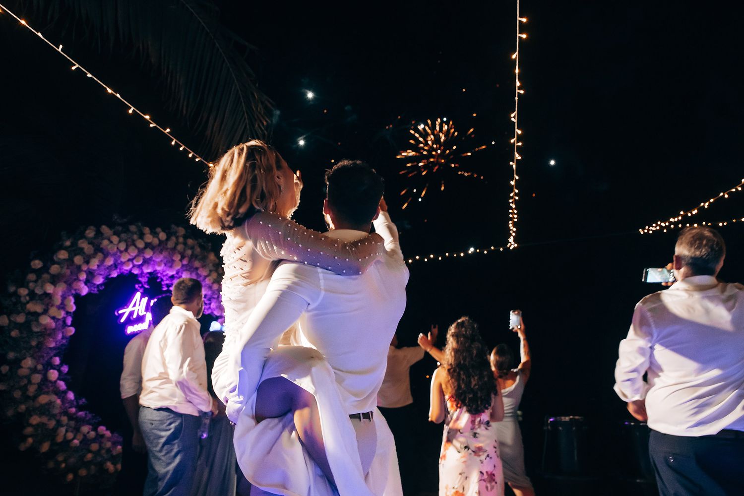 Wedding party celebrates with sparklers during nighttime reception.