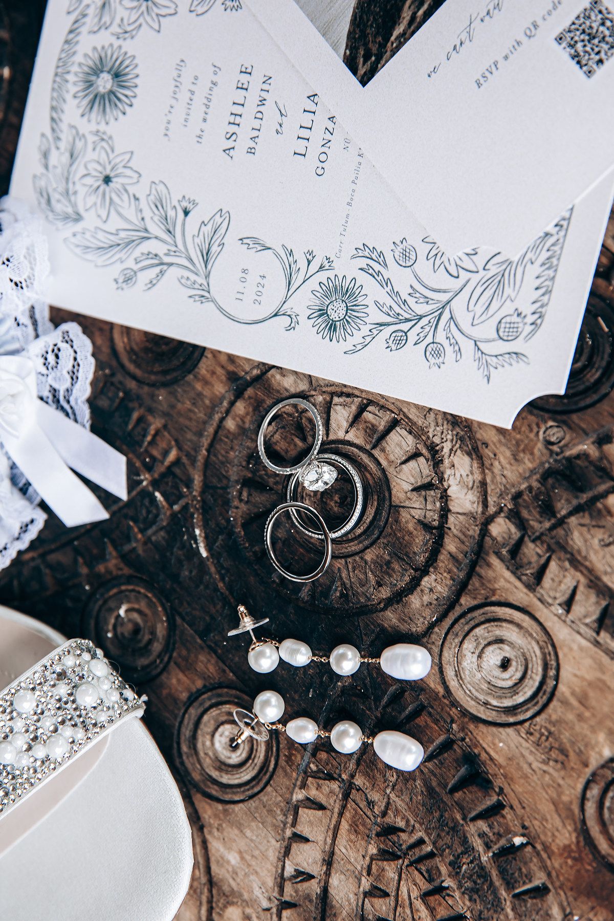 Wedding invitation cards and rings arranged on rustic wooden surface with elegant floral designs and decorative details.