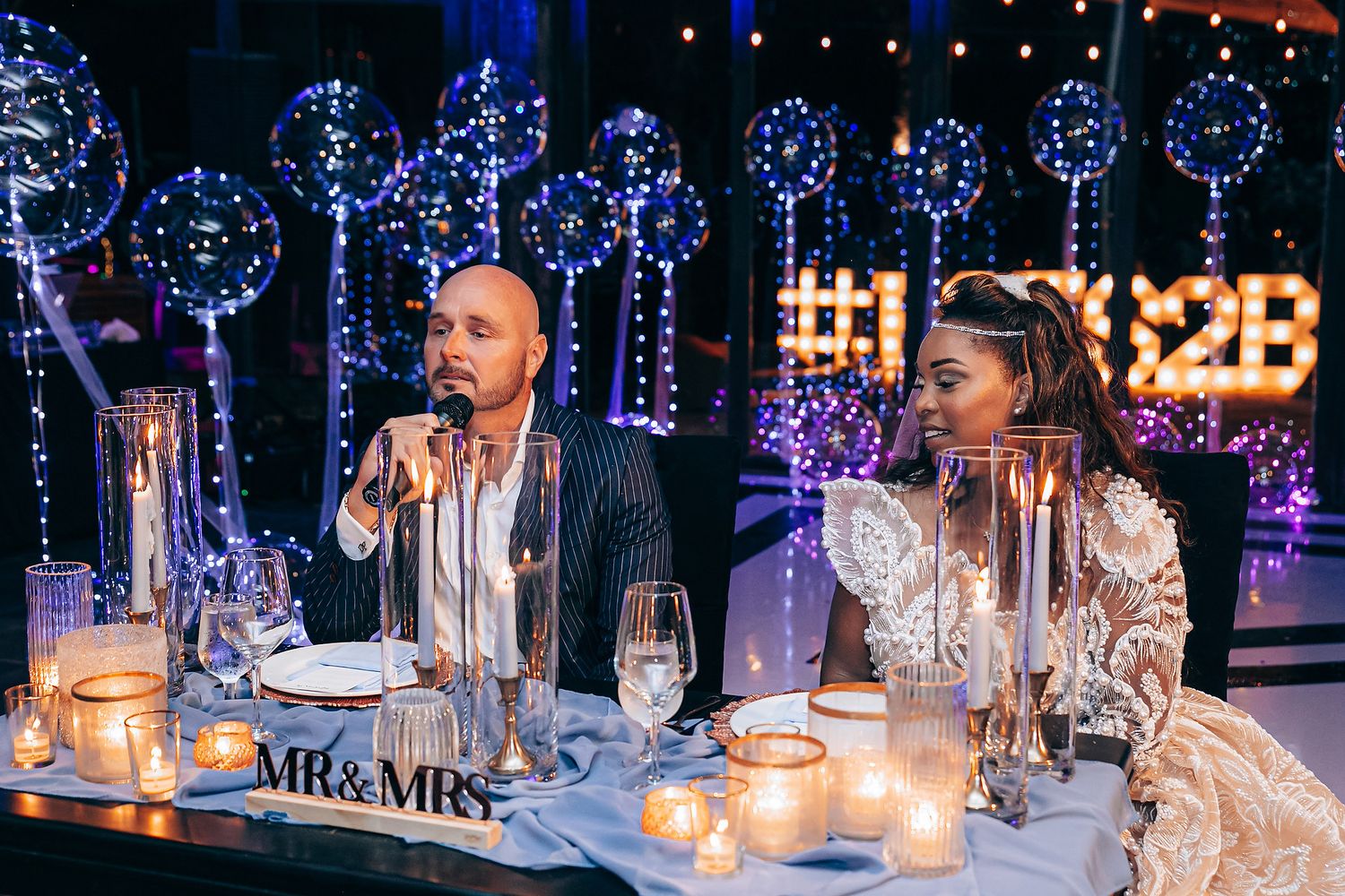 Elegant candlelit table settings with wine glasses and glowing ambiance at an evening reception.