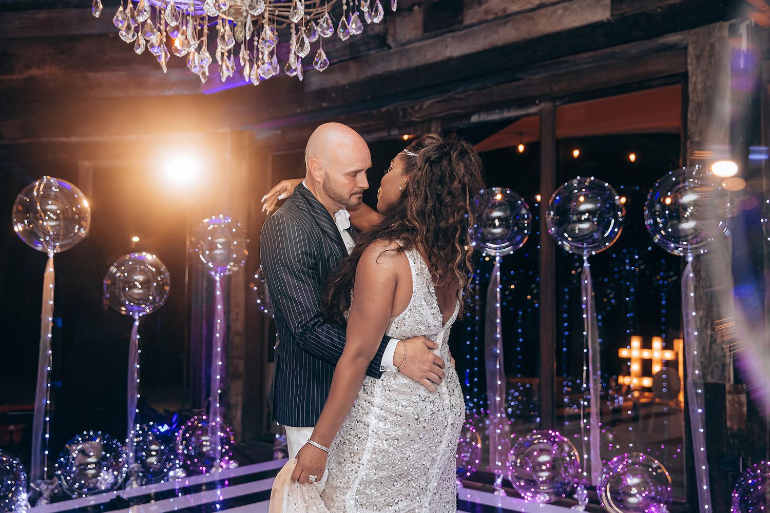Wedding celebration under sparkling chandeliers with purple ambient lighting illuminating the romantic dance scene.