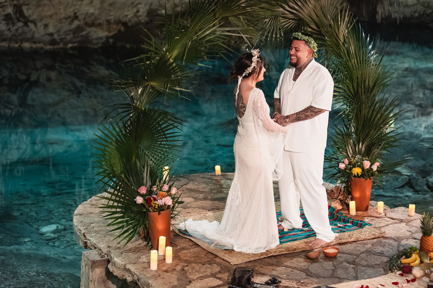 Romantic dinner setup in cave with candles and palm fronds creating tropical atmosphere.