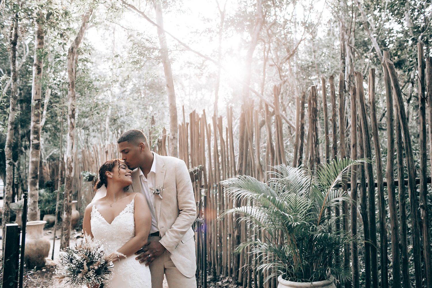 Newlyweds share an intimate moment in a dreamy forest setting with sunlight filtering through the trees.