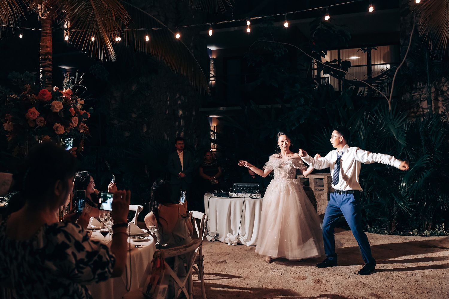 Evening wedding reception under string lights with guests seated at decorated tables.