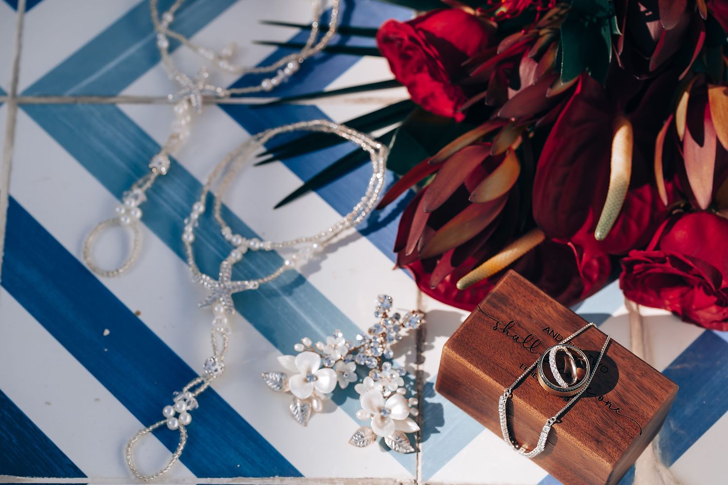 Wedding decorations with red flowers and wooden details arranged on blue and white surface.