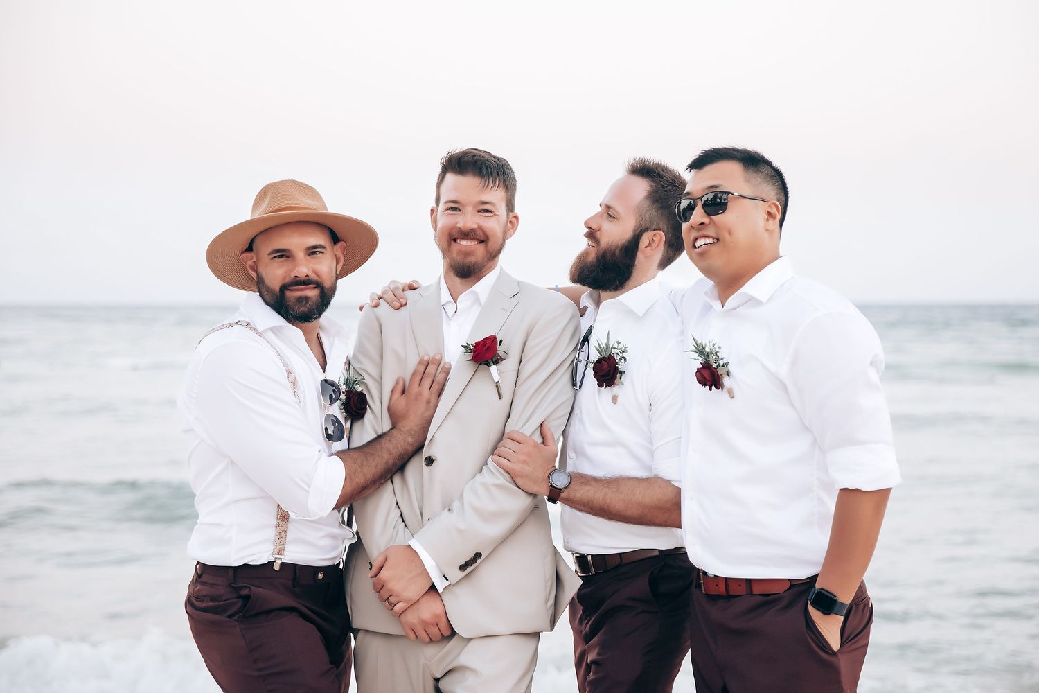 Wedding party in white and beige attire poses on tropical beach.
