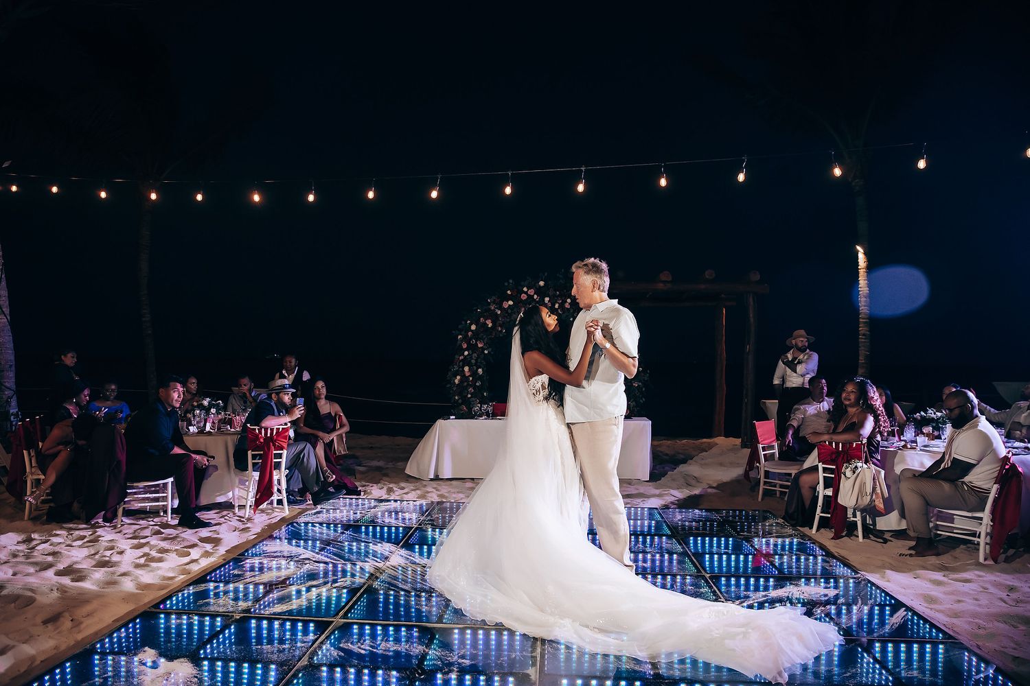 Wedding reception dance floor illuminated with string lights and blue ambient lighting.