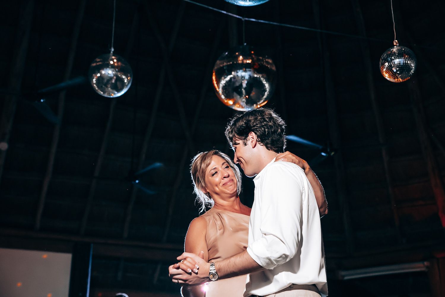 Couple dances intimately beneath glowing disco balls at wedding reception.