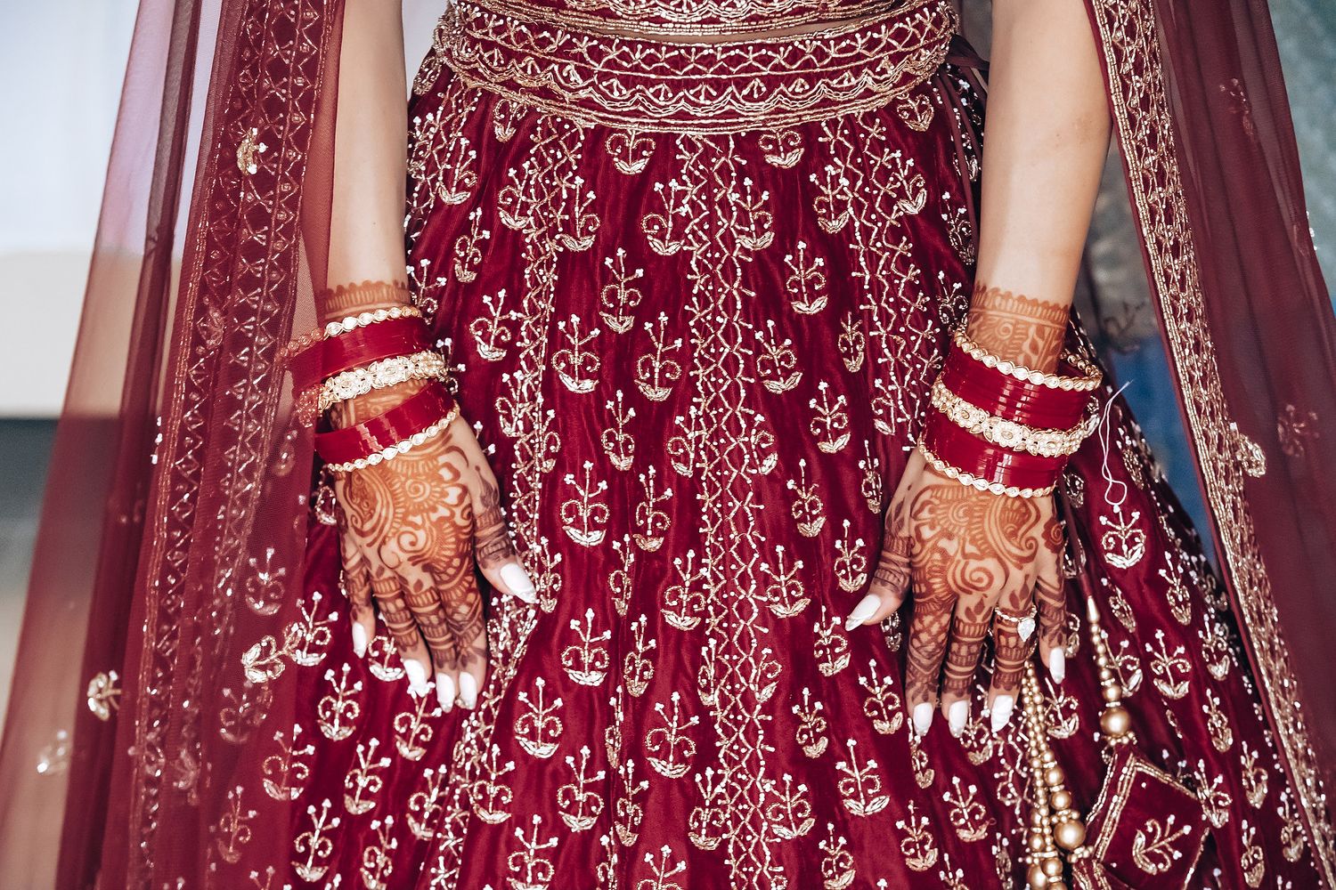 Close-up of ornate red bridal lehenga with detailed embroidery and traditional bangles.