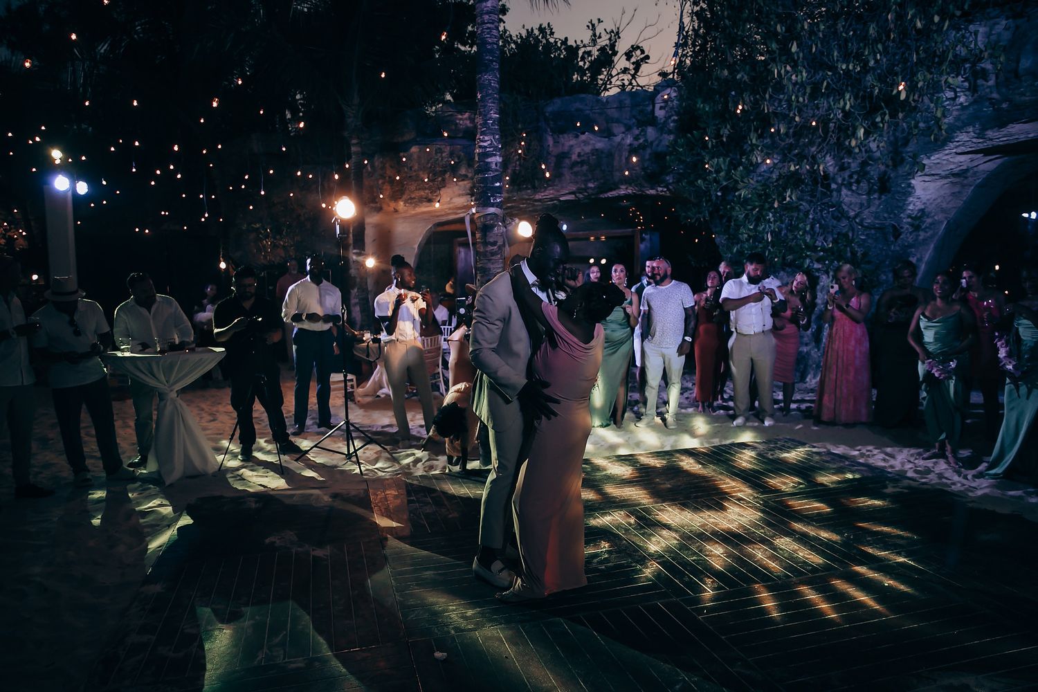 Silhouettes of people dancing at an outdoor nighttime party with colorful lighting and smoke effects.