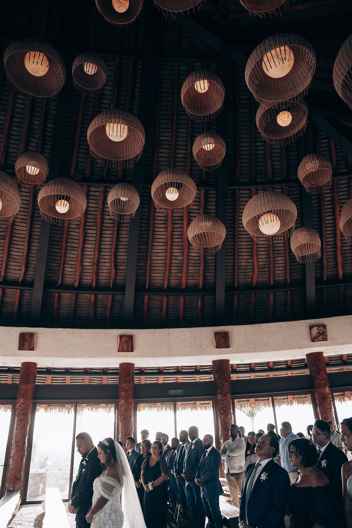 Wedding guests gather under elegant paper lanterns in a circular reception venue with wooden beams.