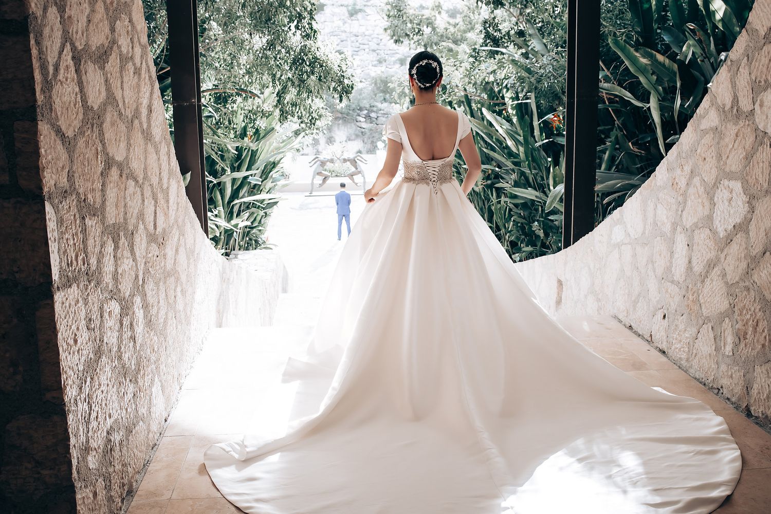 A flowing white wedding dress train creates elegant movement against a stone archway background.