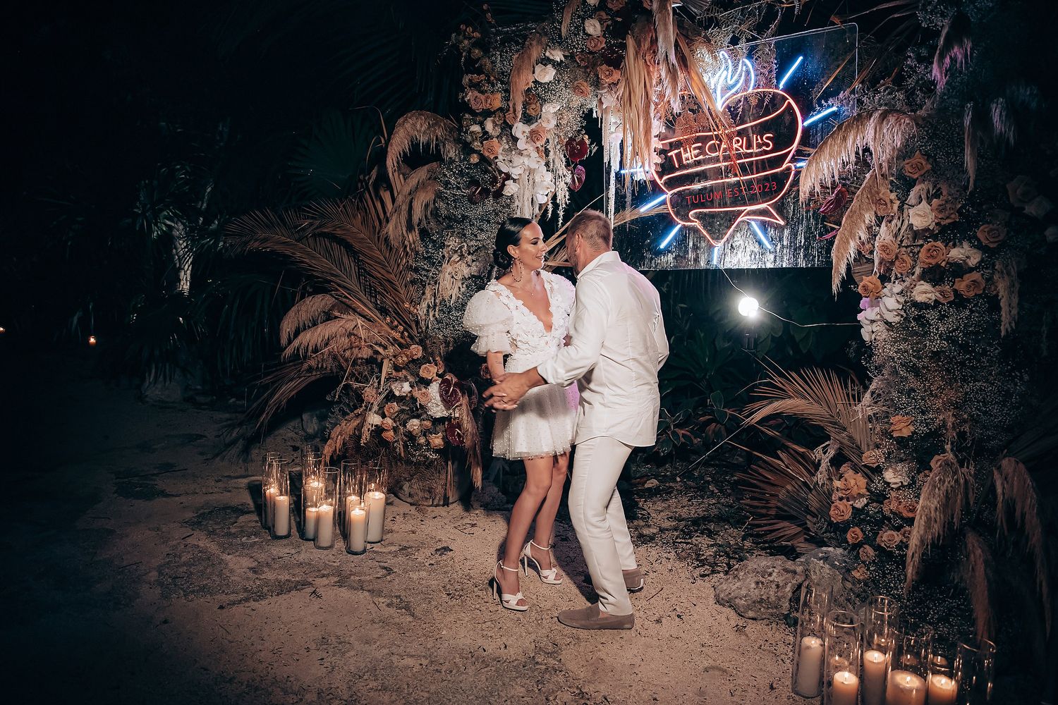 A romantic nighttime wedding celebration with couples dancing under twinkling lights in a tropical outdoor setting.