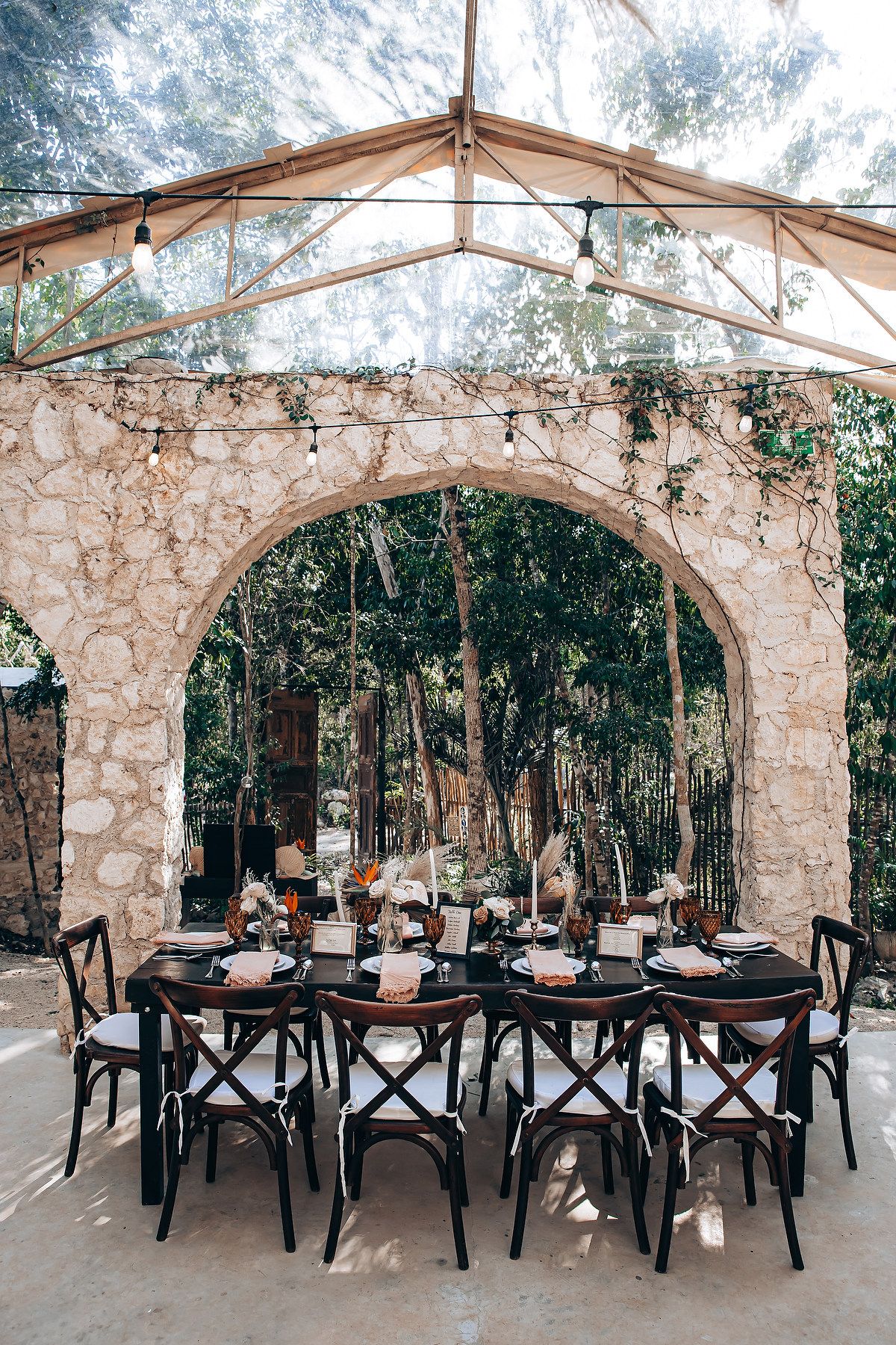 Elegant outdoor wedding reception setup with black chairs and stone archways in a rustic garden setting.