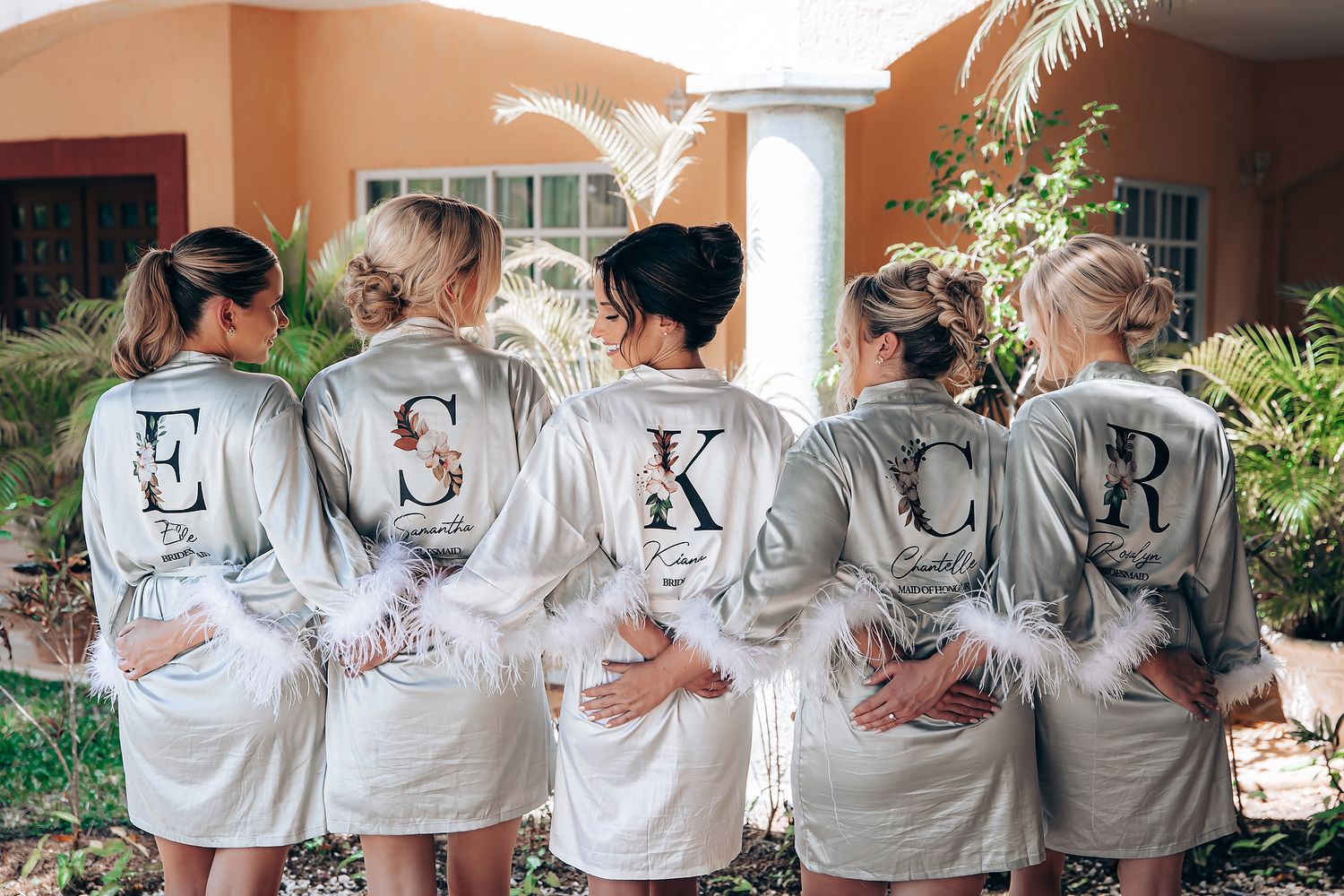 A group of people wearing matching white robes with letters spelling out a word on their backs stand together.