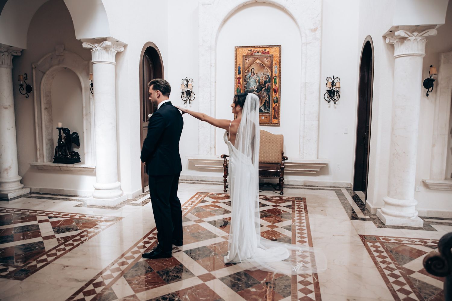 A couple shares a touching moment while standing apart in an elegant church interior with ornate marble columns and patterned floors.