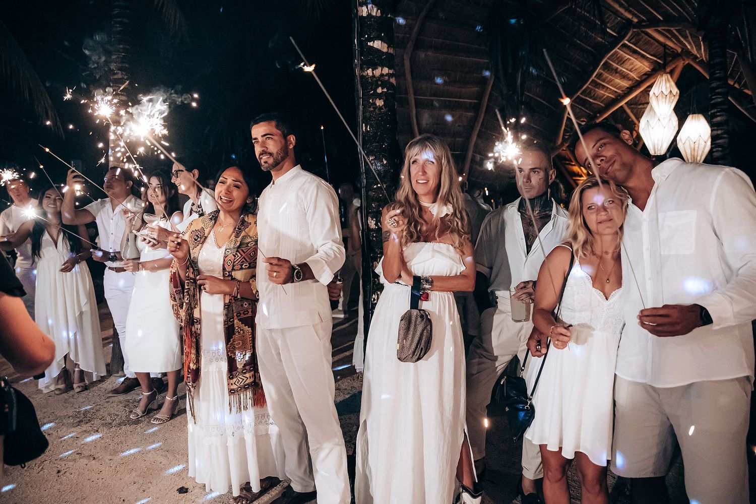 Wedding celebration at night with guests dancing and celebrating in all-white attire.