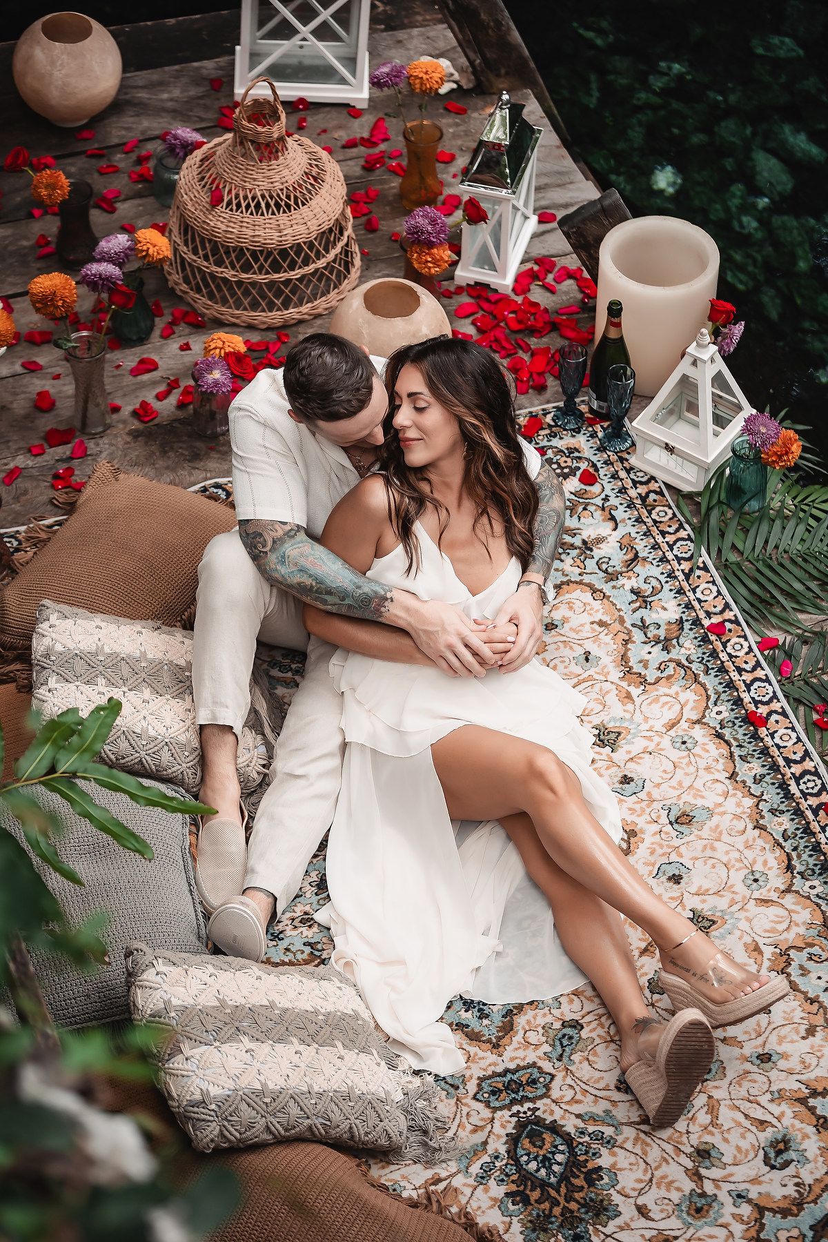 Overhead view of romantic setup with lanterns and rose petals on patterned rug.