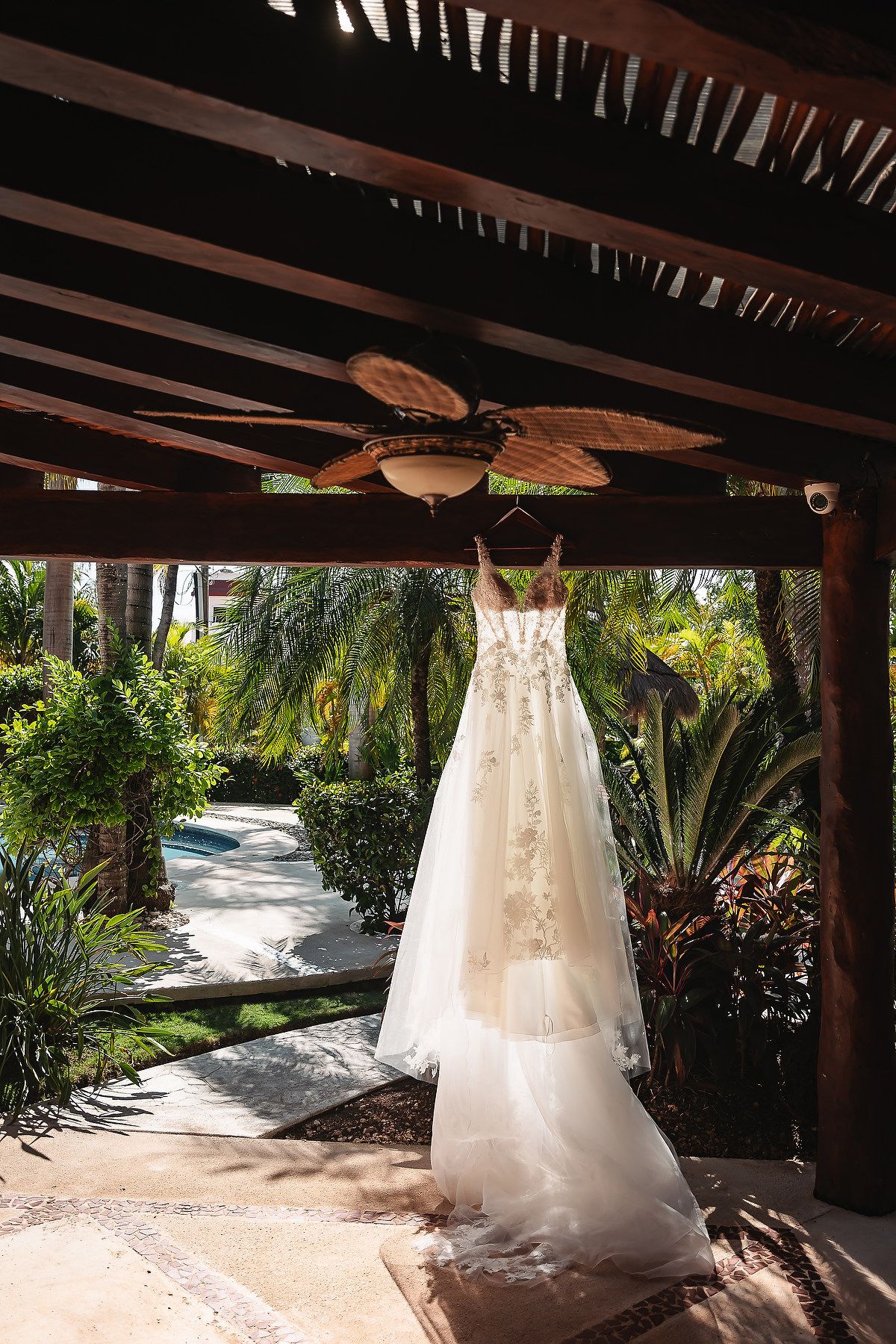 White wedding dress hanging under a wooden pergola with tropical garden in background.