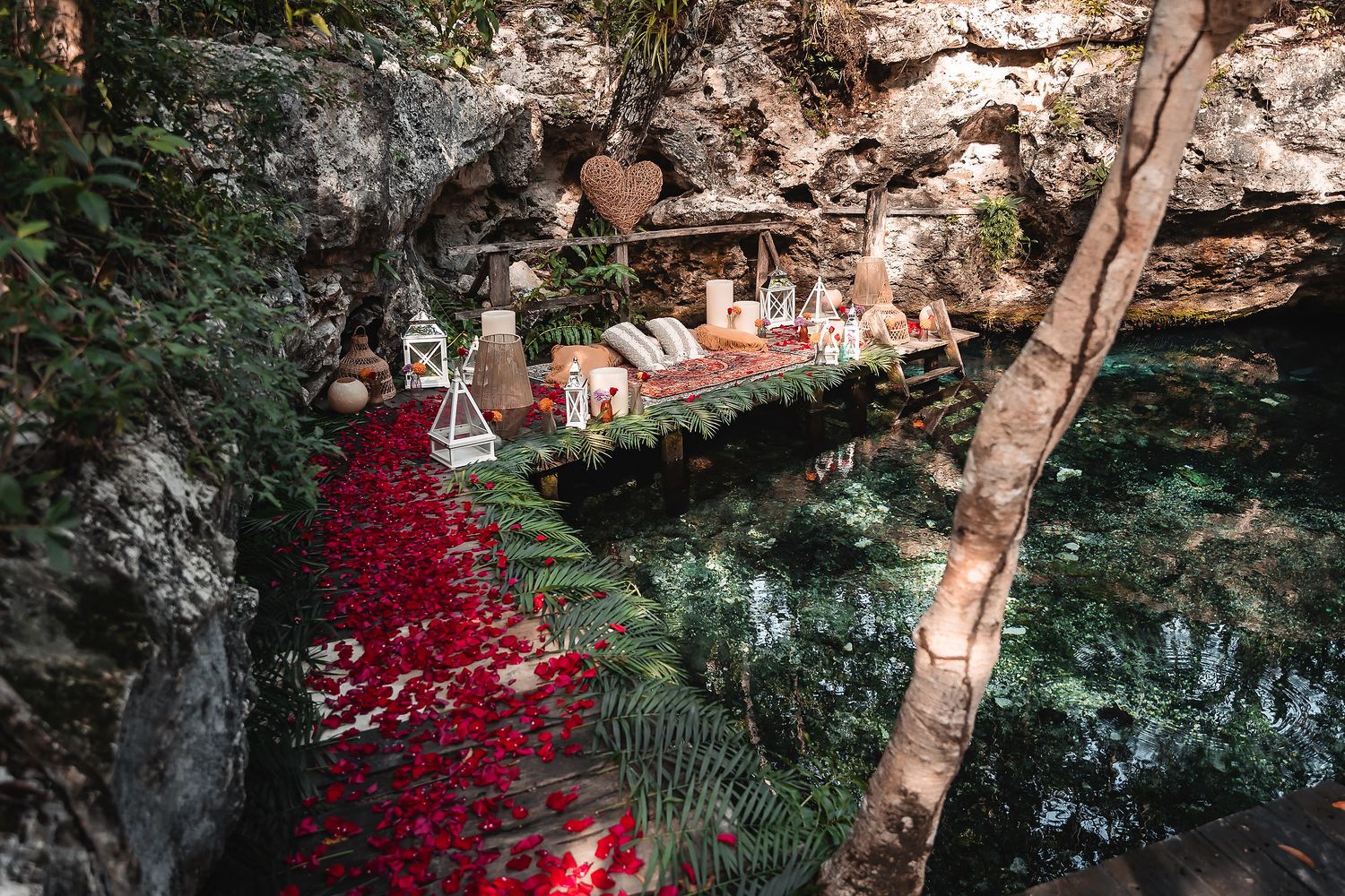 Red rose petals line a romantic picnic setup along limestone cliffs and crystal blue waters.
