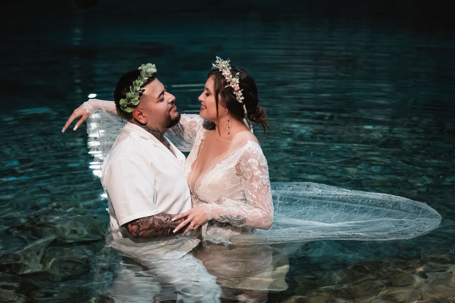 A couple wearing floral crowns shares an intimate moment while standing in crystal clear cenote waters.