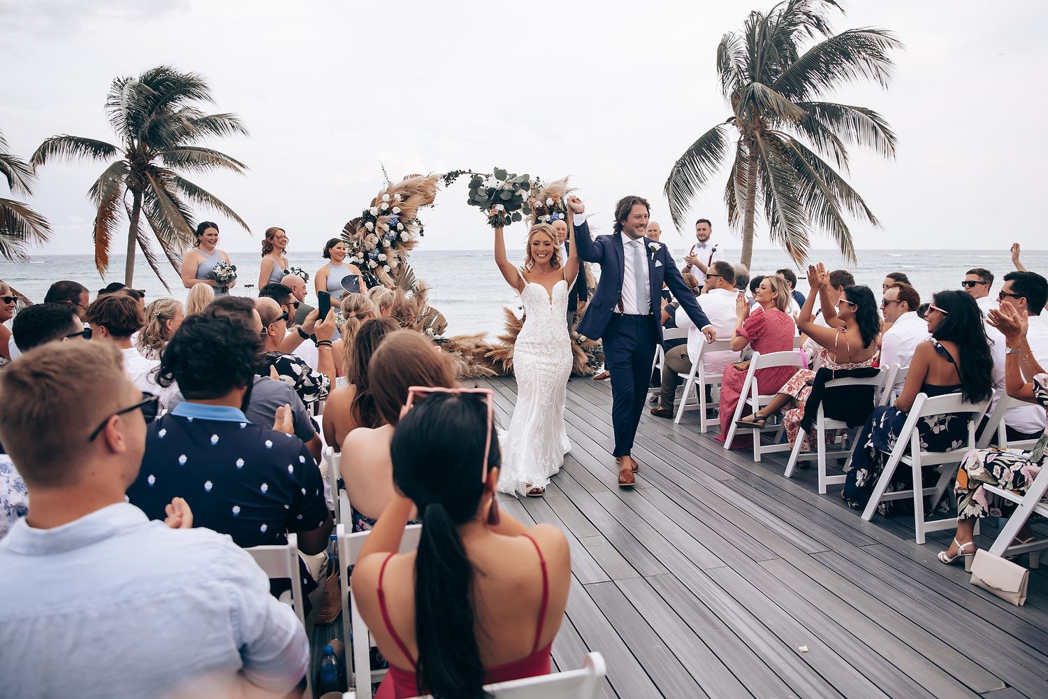 Beachside wedding ceremony on a wooden deck with palm trees swaying in the background.