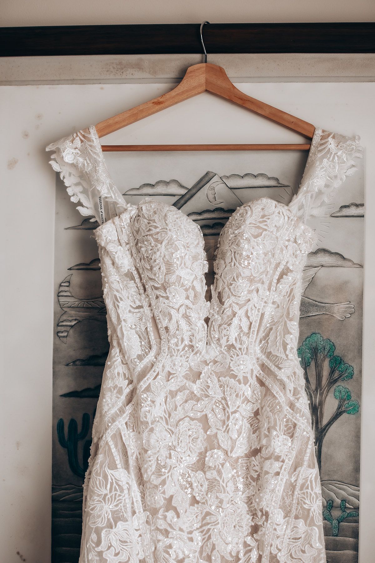 Close-up view of a white lace wedding dress bodice with intricate floral embroidery hanging on a wooden hanger.
